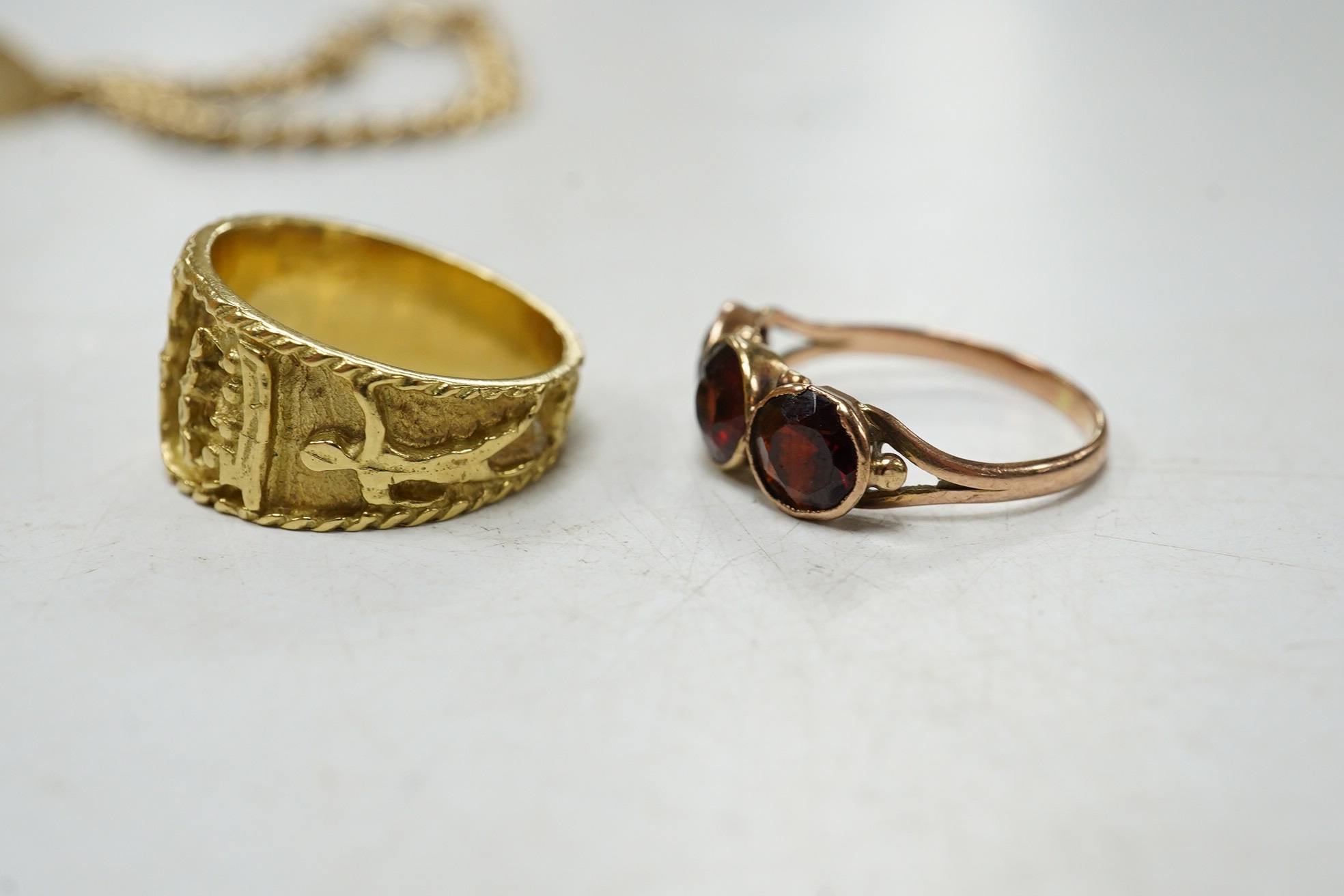 A 9ct curb link identity bracelet, with engraved inscription, 19cm, 12.5 grams, together with a yellow metal Egyptianesque ring and a yellow metal and three stone garnet set ring. Condition - fair